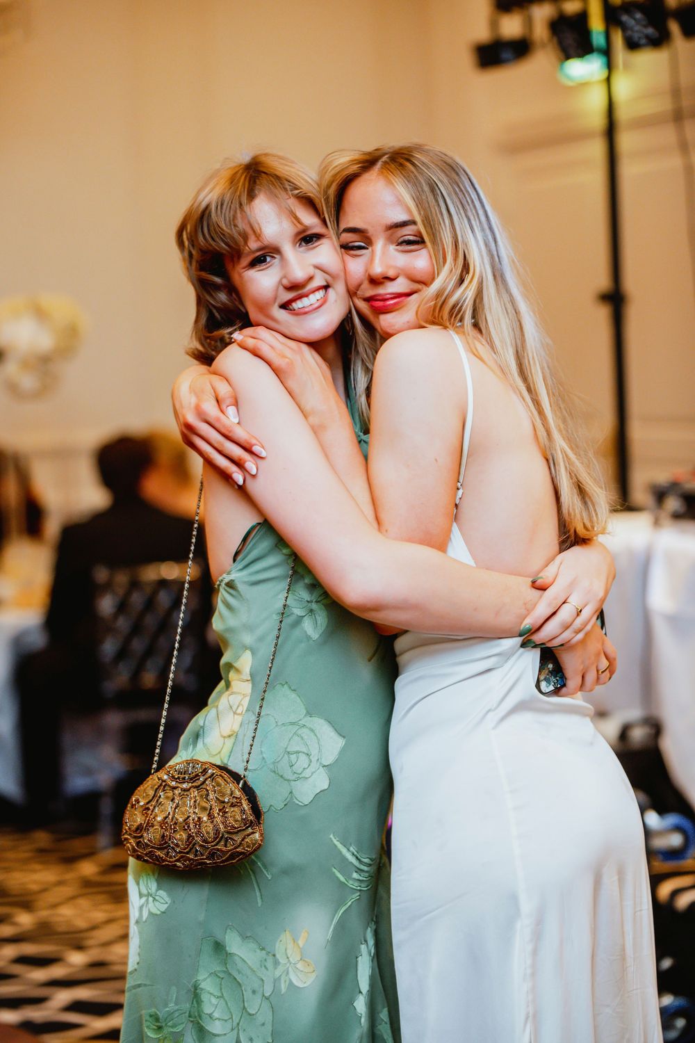 Bridesmaids in mint green dresses embrace warmly during wedding reception moments.
