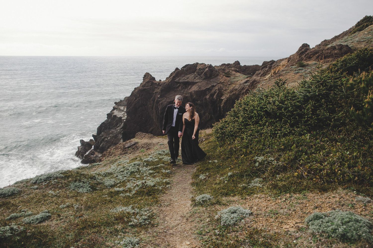 Two people stand on a scenic coastal trail overlooking rugged cliffs and the ocean in Northern California.