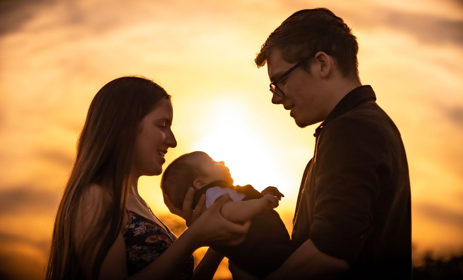 Silhouette of parents holding baby against golden sunset backdrop.