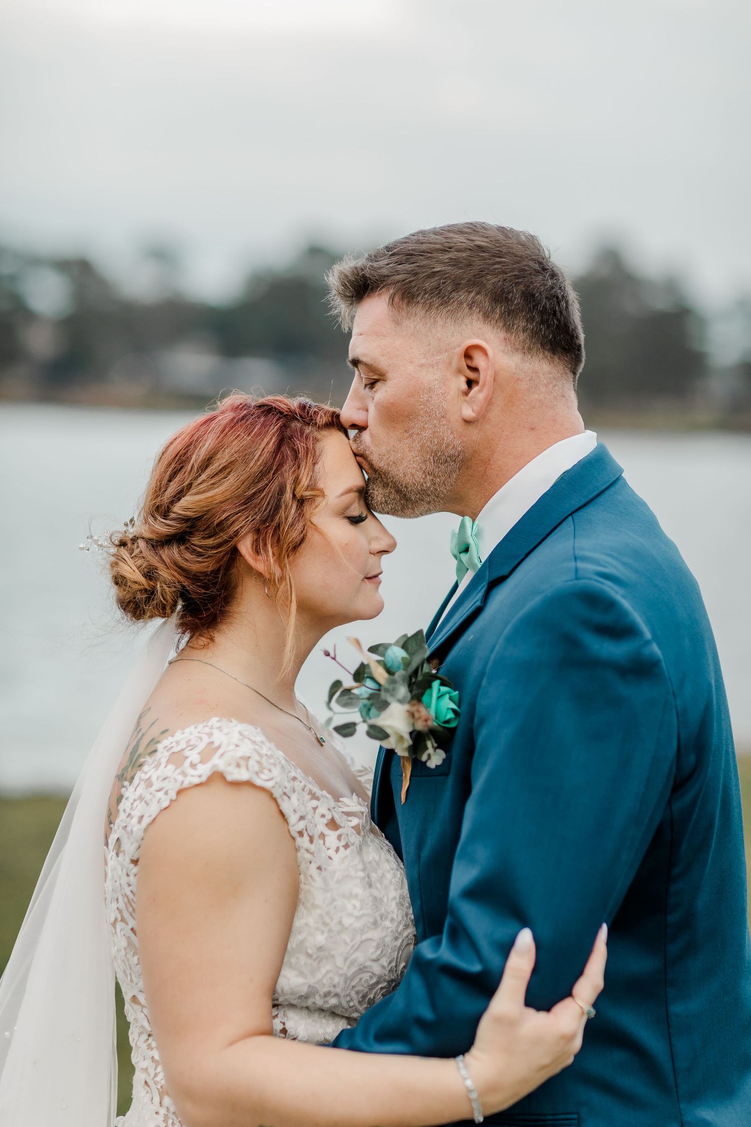 Romantic wedding couple in navy suit and lace dress share intimate moments by the waterfront.