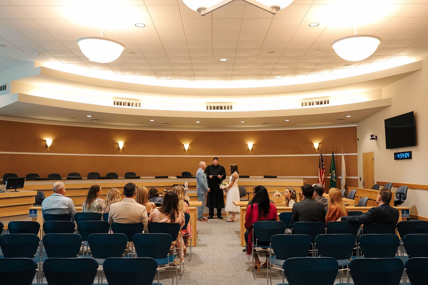 Low-angle view of an auditorium interior with curved walls, ceiling lights, and rows of blue seats during a gathering.