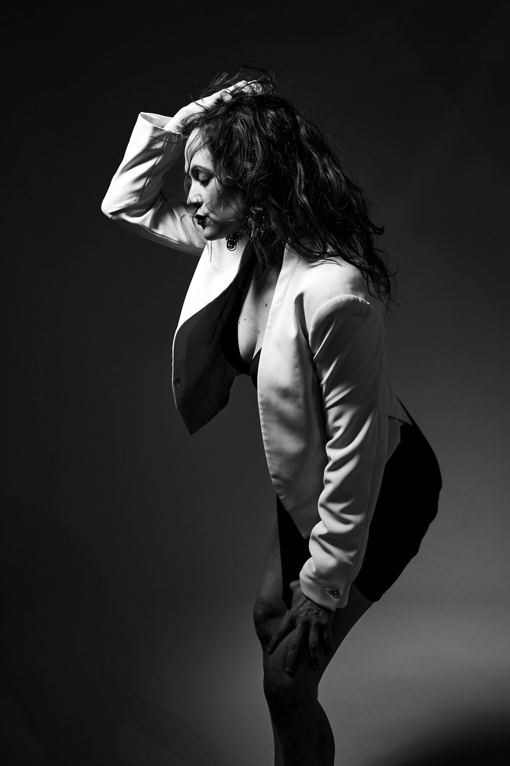 Dramatic black and white portrait of a dancer in a white blazer striking an artistic pose against dark background.