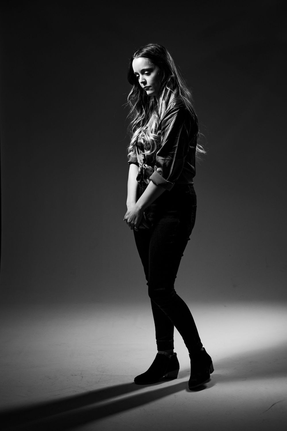 Black and white dramatic photos of a person in dark clothing casting shadows on a spotlight-illuminated floor.