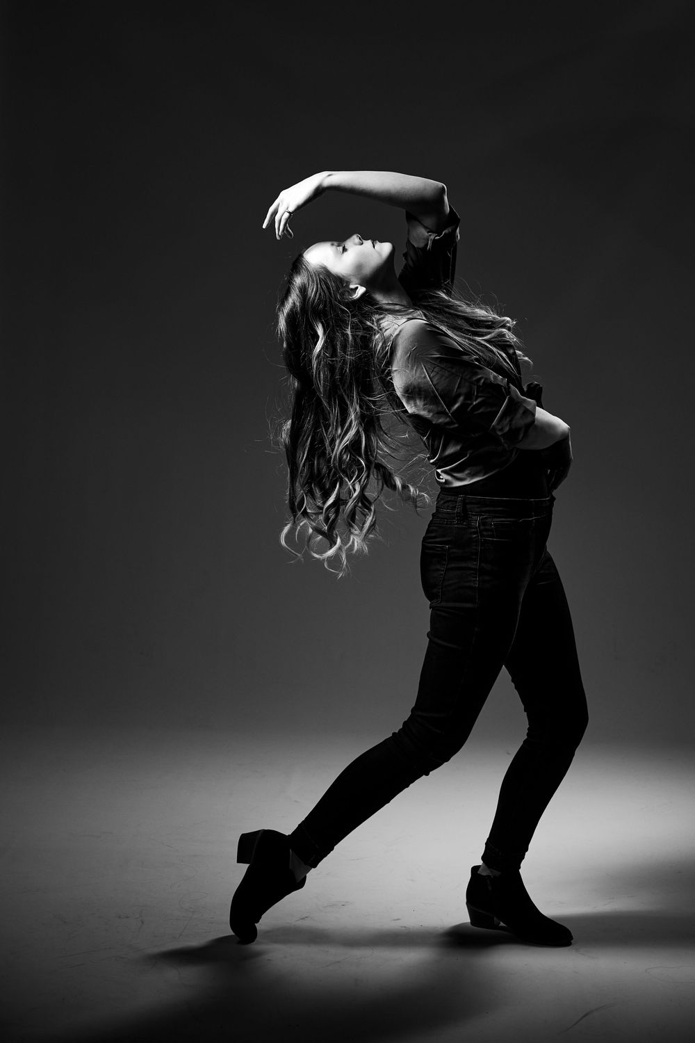 Black and white portrait of a dancer arching backwards with flowing hair in a dramatic contemporary dance pose.