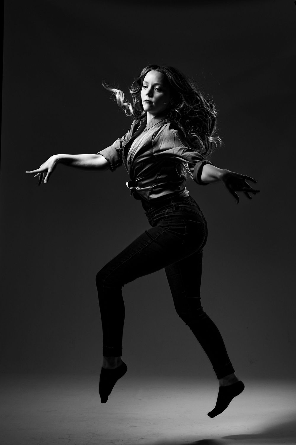 A dramatic black and white photo of a dancer leaping gracefully in a dark outfit against a simple background.