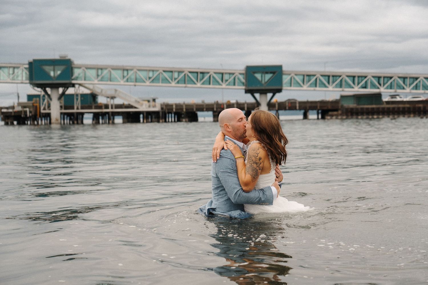 A couple shares a playful moment while frolicking in the ocean waves on a cloudy day at the beach.