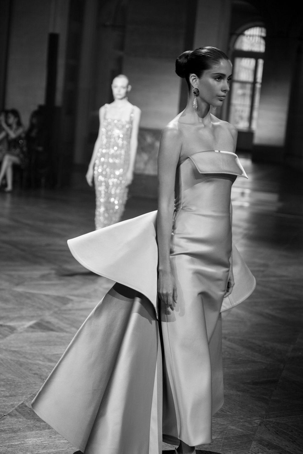 Models showcase sculptural white avant-garde dresses with dramatic architectural details on a dark runway.