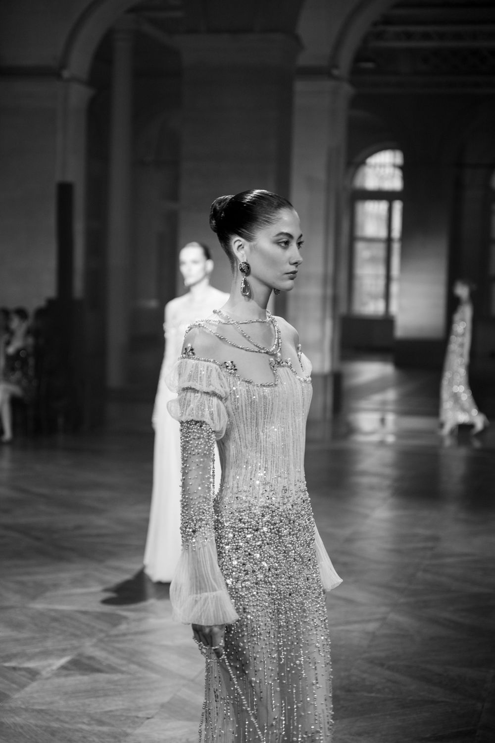 Black and white fashion photo showcasing elegant beaded gown with delicate fringe details on runway.