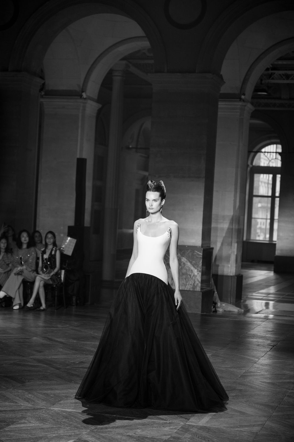 A model presents a striking black and white ballgown against architectural arches in black and white photography.