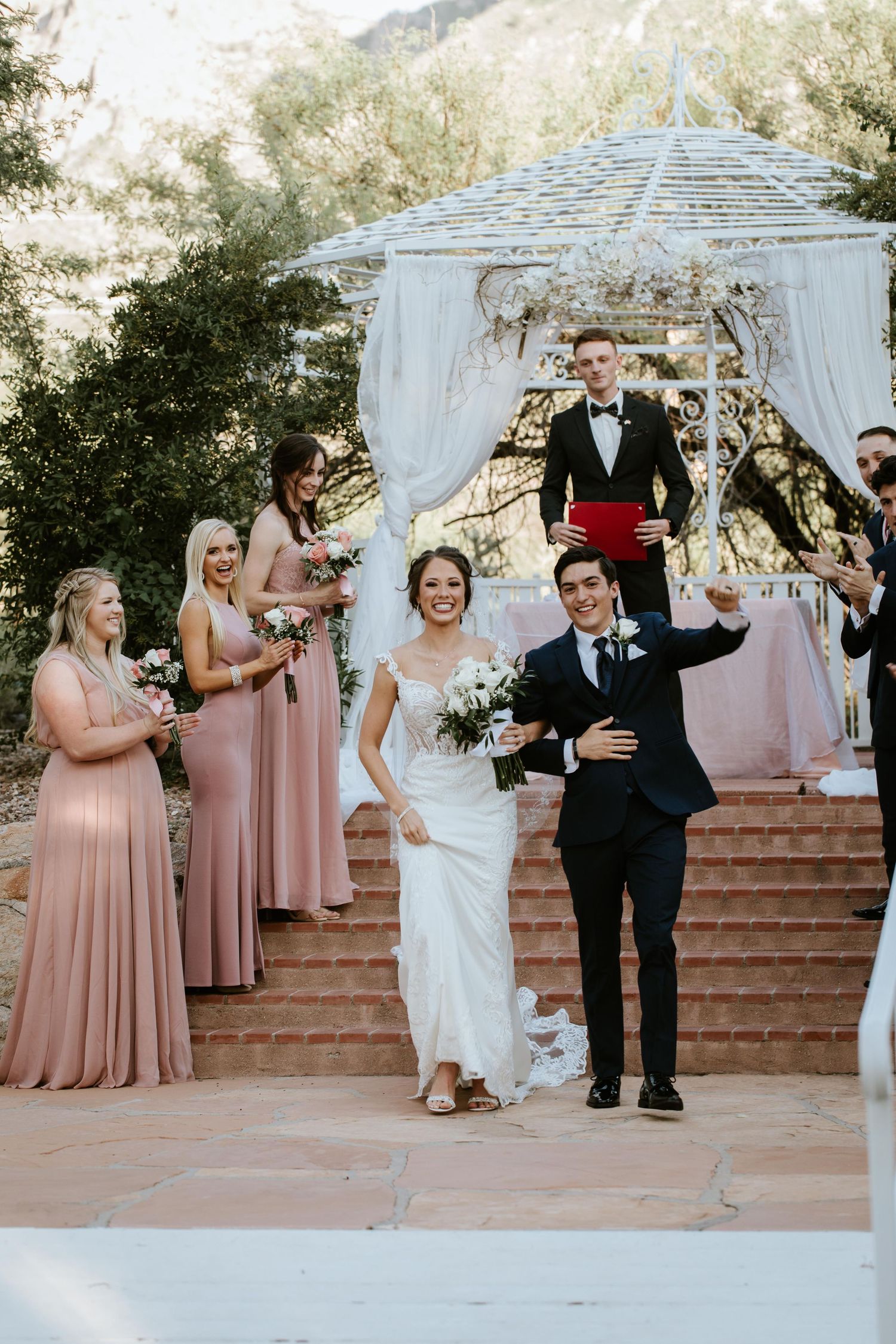 Newlyweds descend elegant stone steps  beneath a draped white gazebo at outdoor ceremony at saguaro buttes wedding venue in tucson arizona