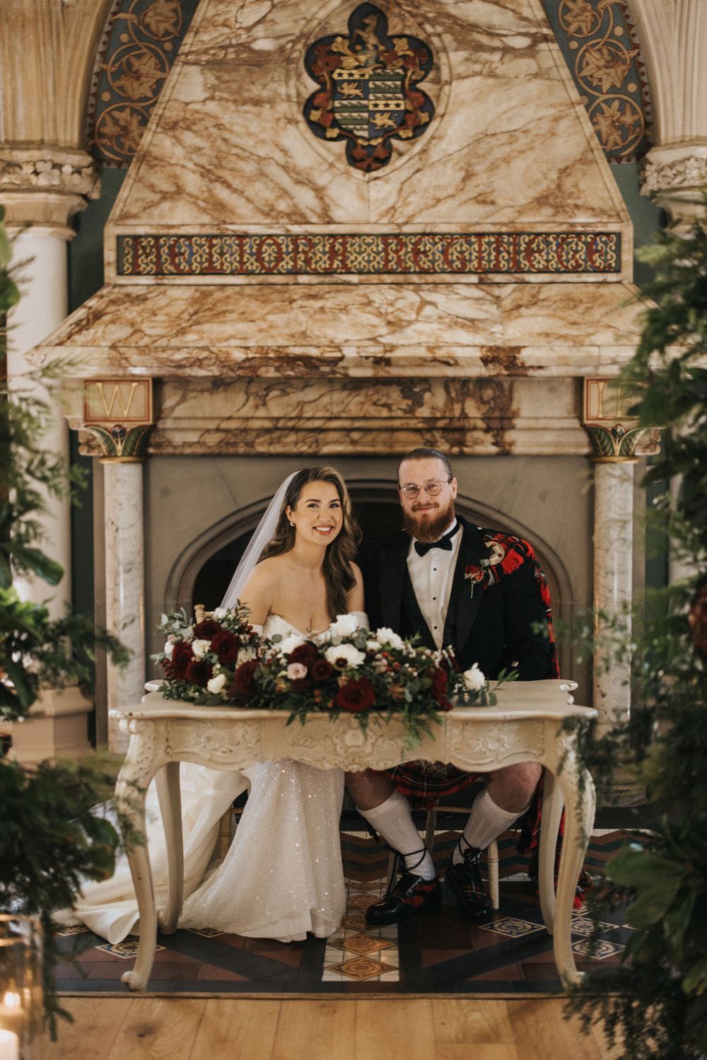 A couple sits together at an elegant ornate table decorated with florals for their wedding ceremony at a grand venue.