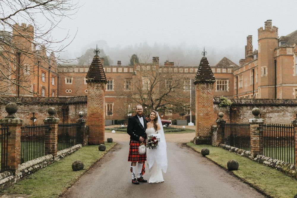 A bride and groom walk through the grounds of a historic brick castle estate on their winter wedding day.
