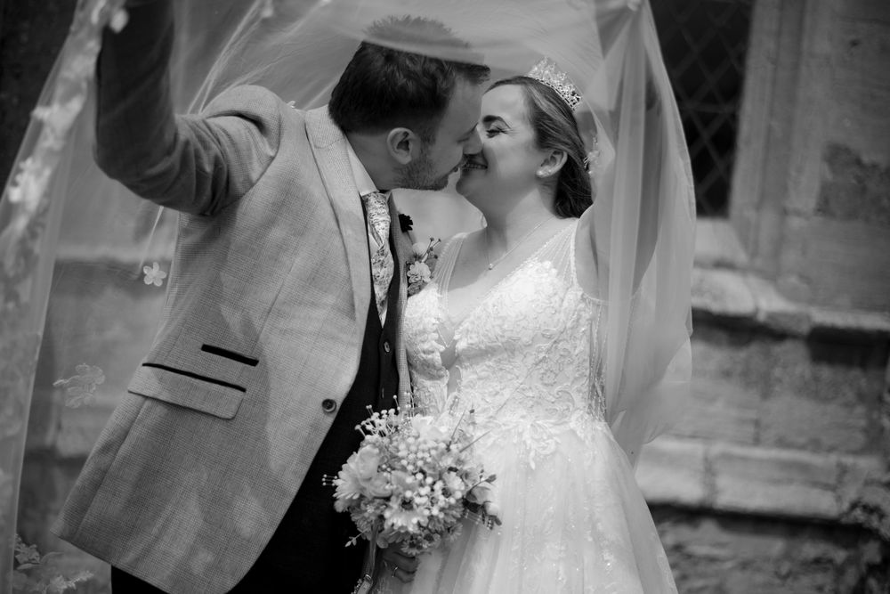 A tender wedding moment captured in black and white with a flowing veil and delicate bouquet.