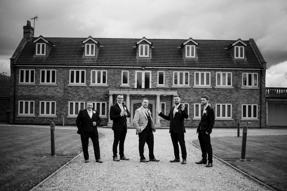 Five people in formal attire stand in front of a traditional brick building with dormer windows.