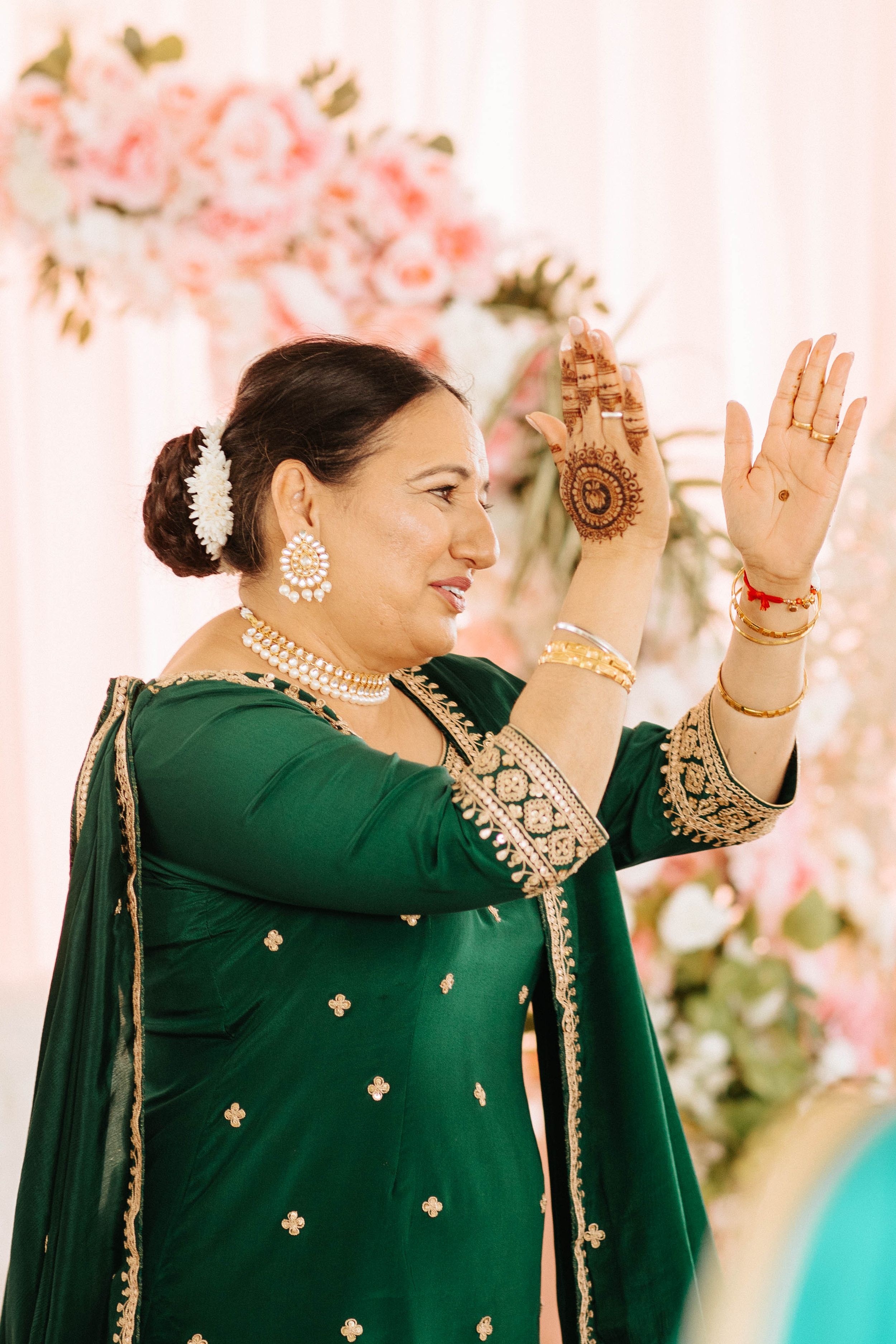 Traditional Indian wedding attire featuring emerald green suit with gold embellishments, pearl jewelry and mehndi decorated hands.