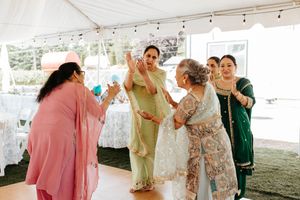 Multiple people celebrate and dance together in casual attire under a large outdoor tent at a special event.
