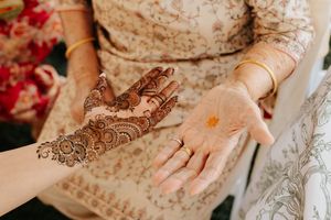 Intricate henna design being applied on hands with traditional mehndi patterns against light colored fabric background.
