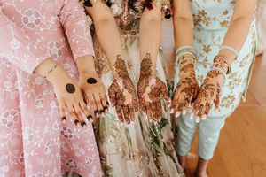 Close-up details of intricate henna designs on hands and feet showcased against a pink backdrop with gold accents.