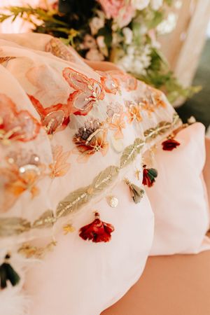 Delicate floral embroidery details on white fabric with pink, orange and red flowers in soft, romantic lighting.