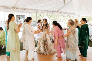 Wedding guests gather under a white tent canopy, dancing and celebrating at an outdoor reception.
