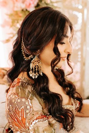 A detailed side profile view showing ornate gold chandelier earrings and wavy dark hair with delicate hair accessories.