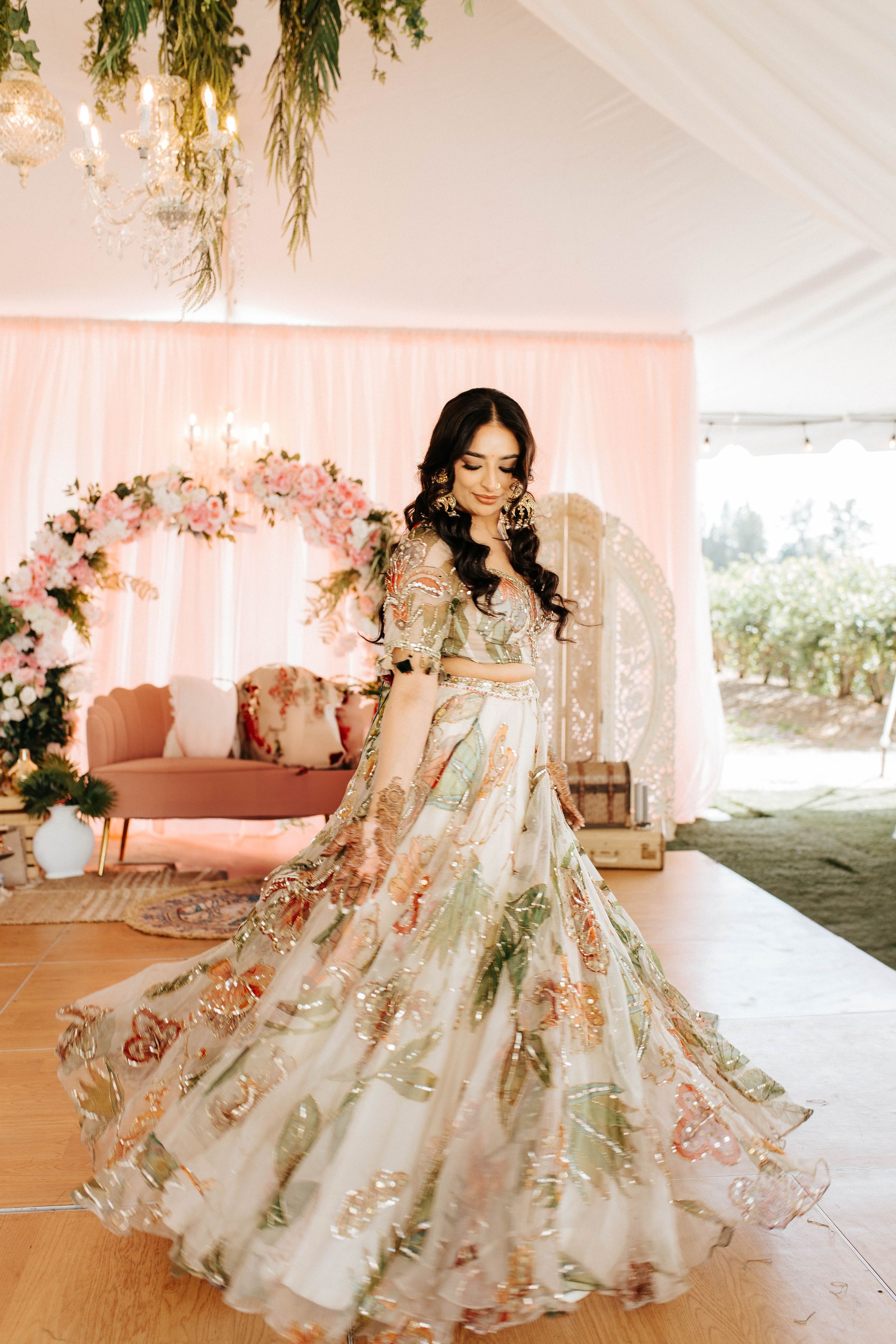 A stunning floral wedding lehenga with intricate embroidery twirls in a pink-decorated venue setting.