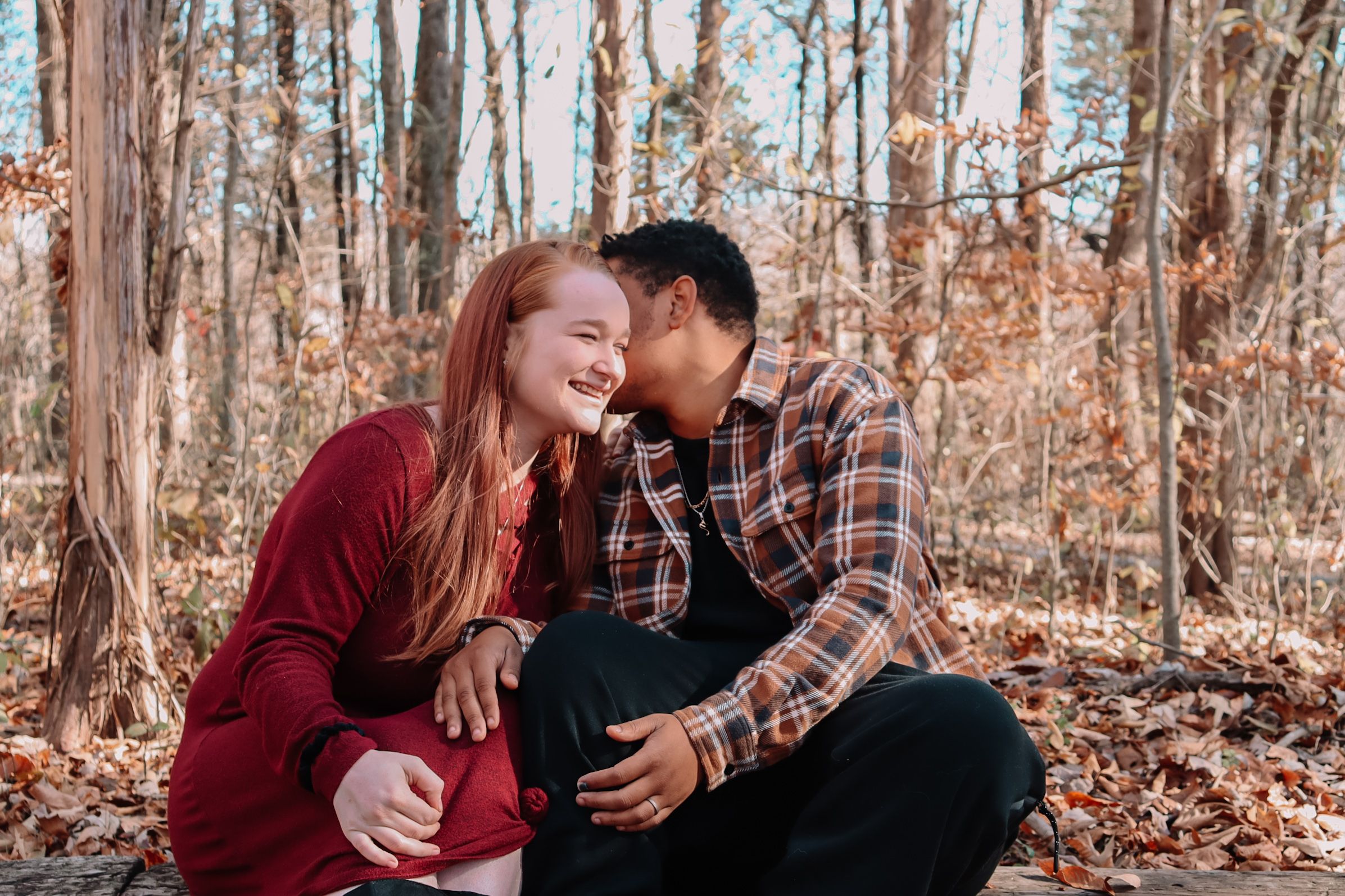 Couple in casual attire sharing intimate moments among autumn trees in wooded setting.