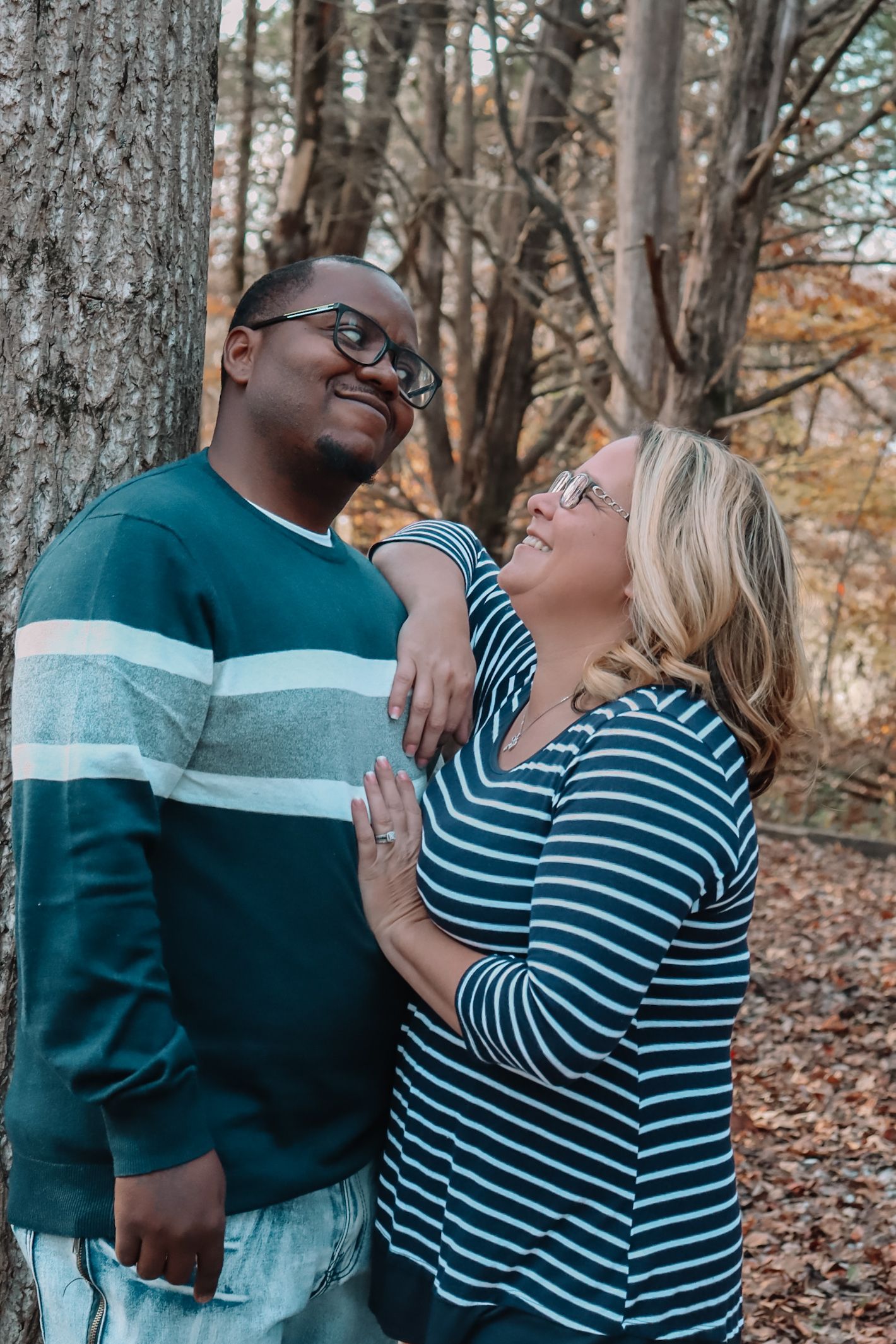 Couple in striped and solid shirts sharing tender moments against tree backdrop in woods.