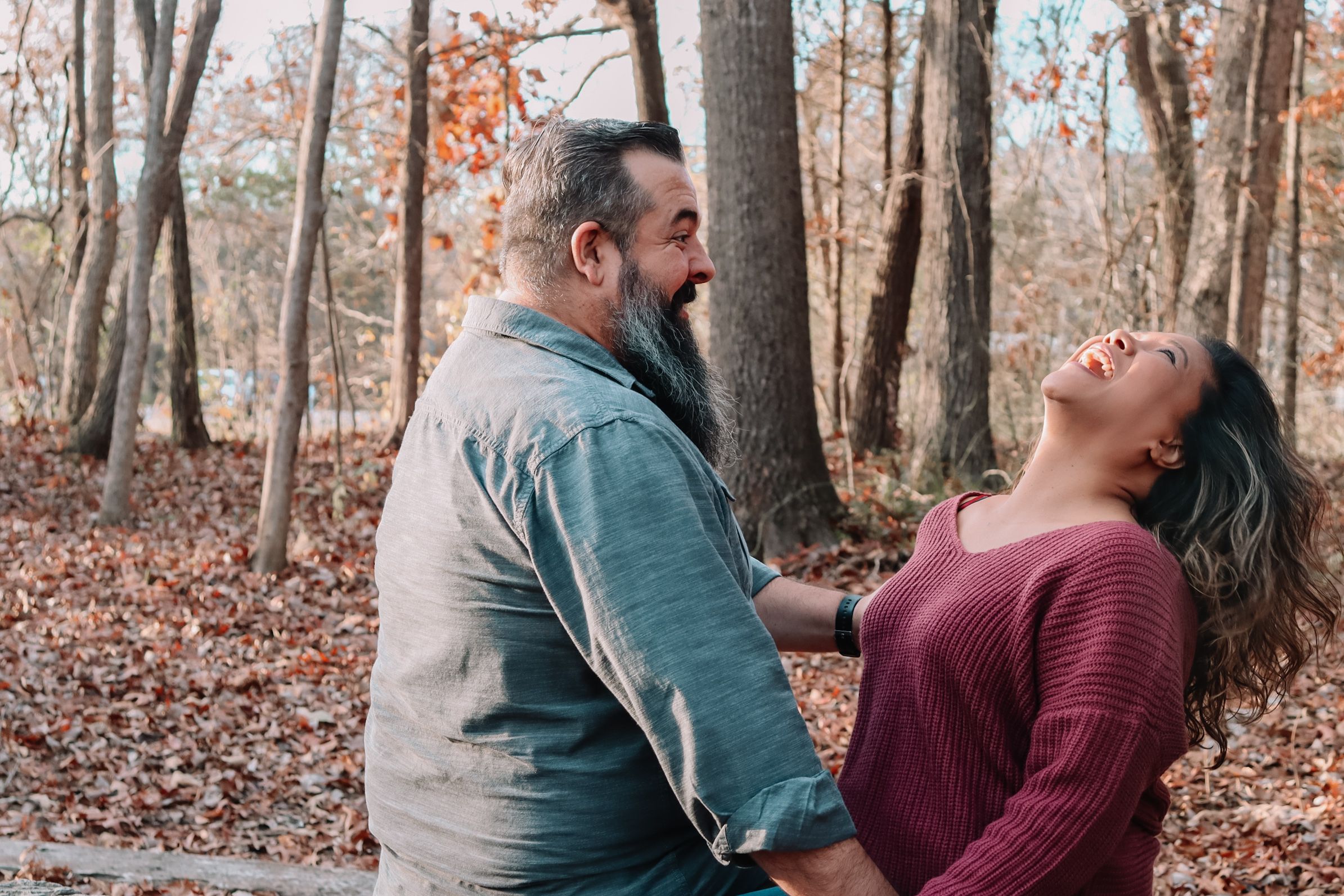 Couple in casual wear sharing intimate moment among fallen leaves in autumn forest.