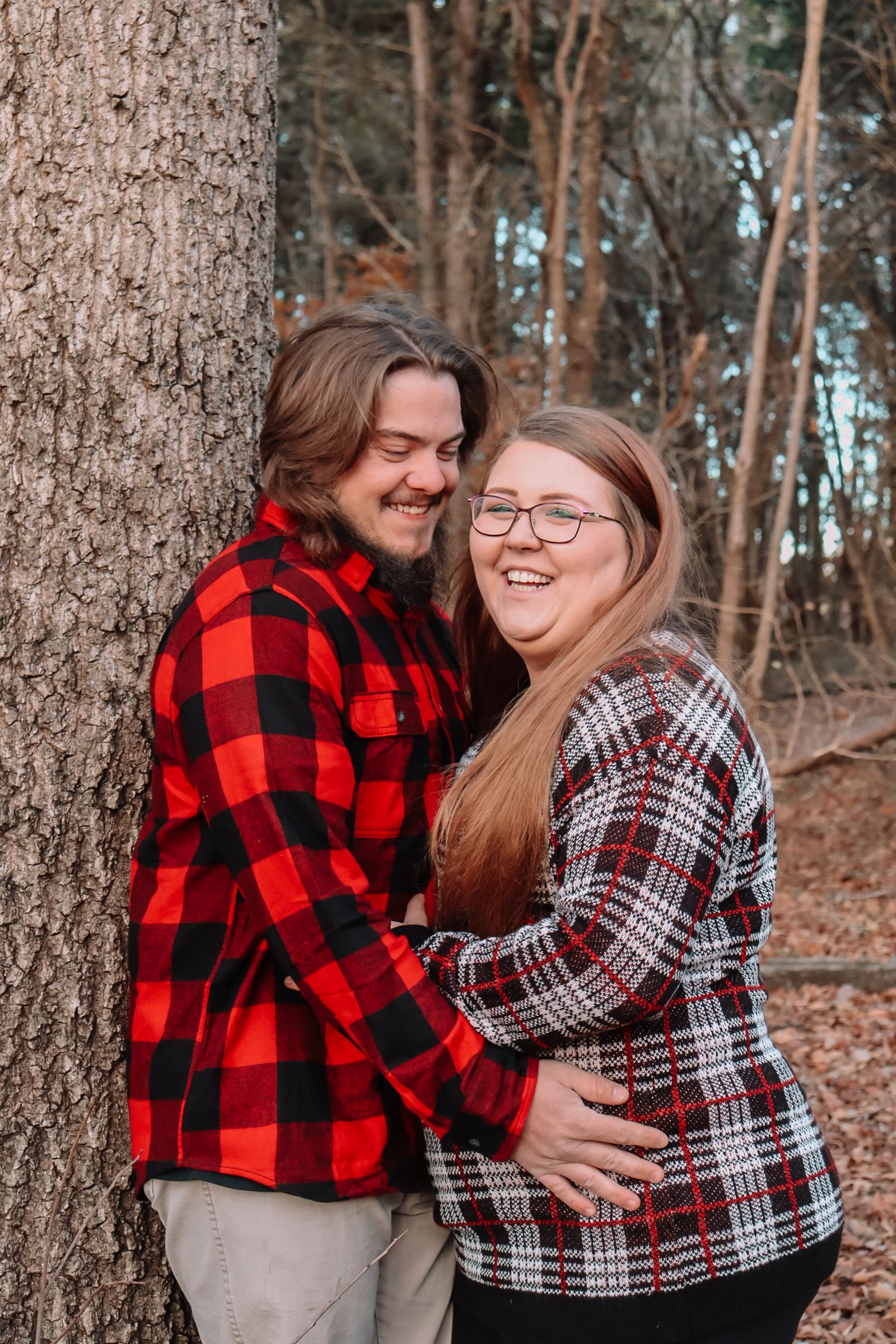 Couple in plaid shirts embracing and laughing together in wooded autumn setting.