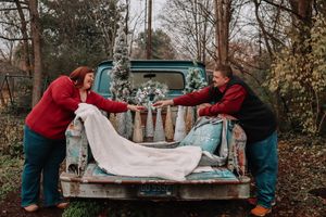 Couple in red plaid shirts posing playfully on vintage pickup truck bed in autumn setting.