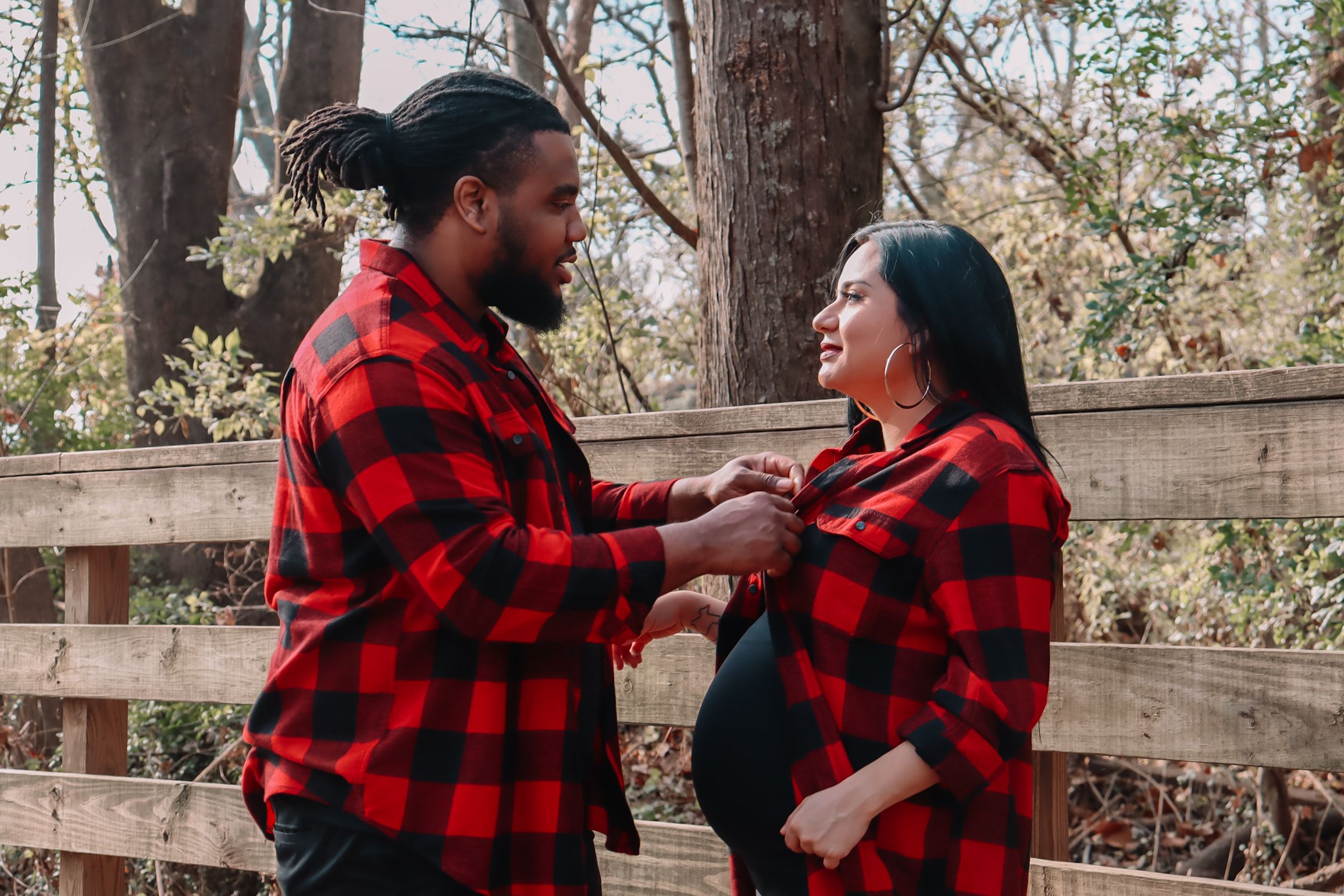 Couple in matching buffalo plaid shirts playfully interacting in outdoor forest setting.