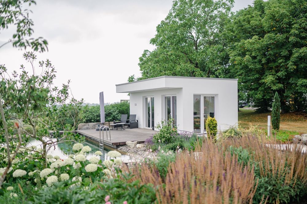 Modernes weißes Haus mit natürlicher Landschaftsgestaltung und Gartenelementen.
