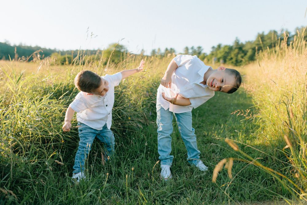 Two children playing and bending over in a tall grass field on a sunny summer day.