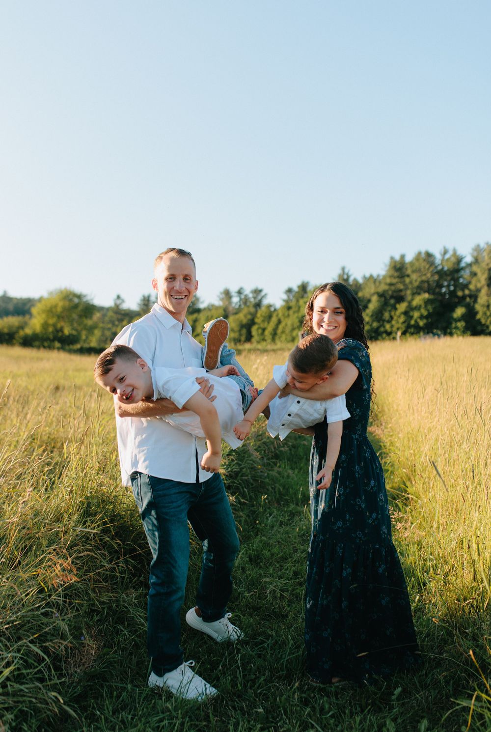 A family plays and laughs together in a golden field at sunset.