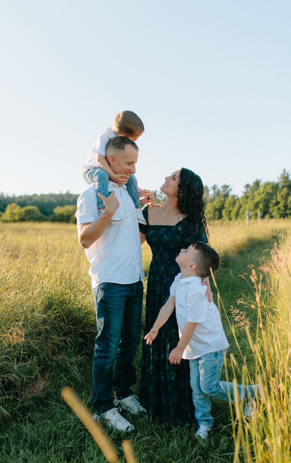 A family shares joyful moments together in a sunlit meadow with tall grass during golden hour.