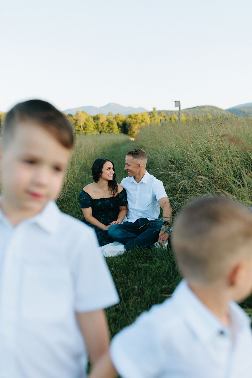 A family lounges together in a scenic mountain meadow filled with tall grass during golden hour.