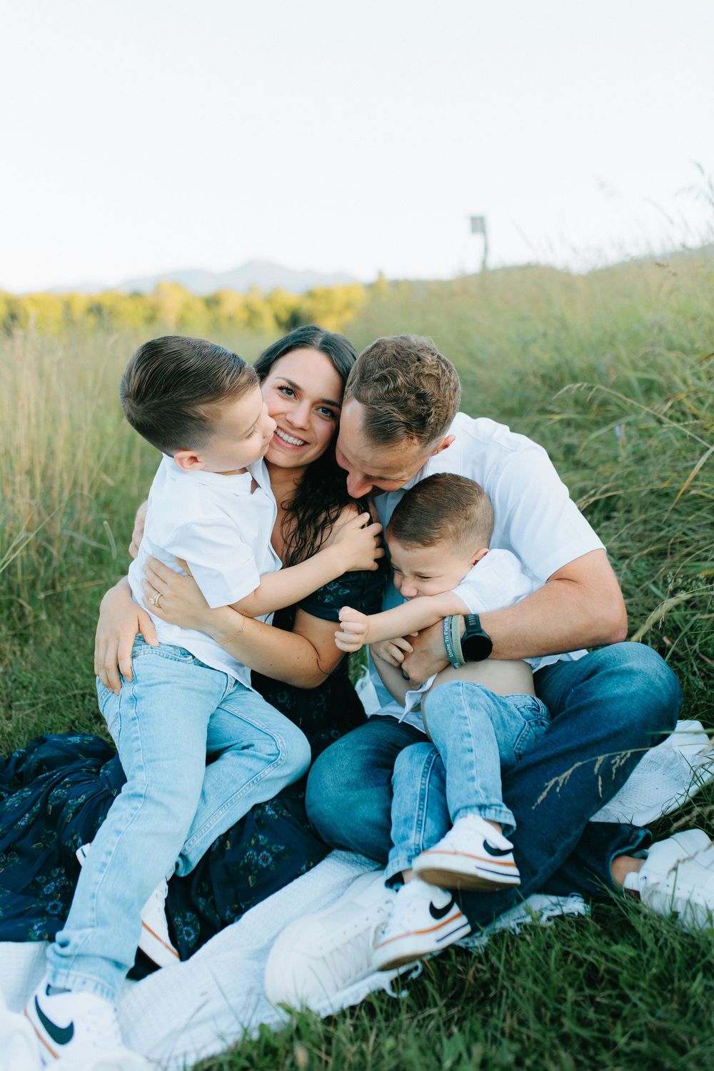 A loving family embraces while sitting together in a grassy field on a sunny afternoon.