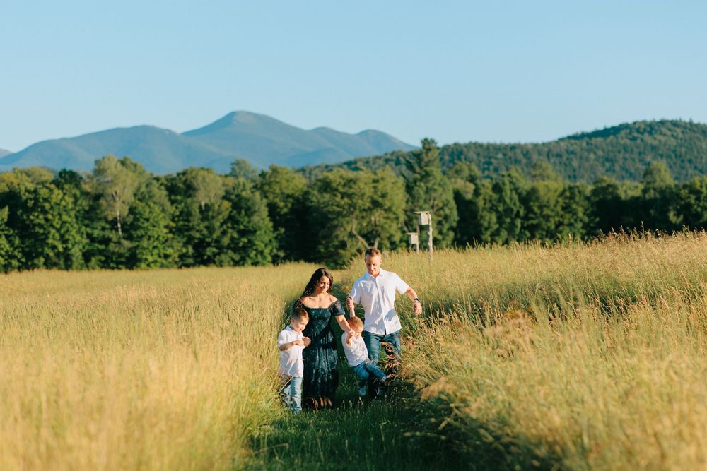 A family walks through a golden summer meadow with mountains and forests in the distance on a sunny day.