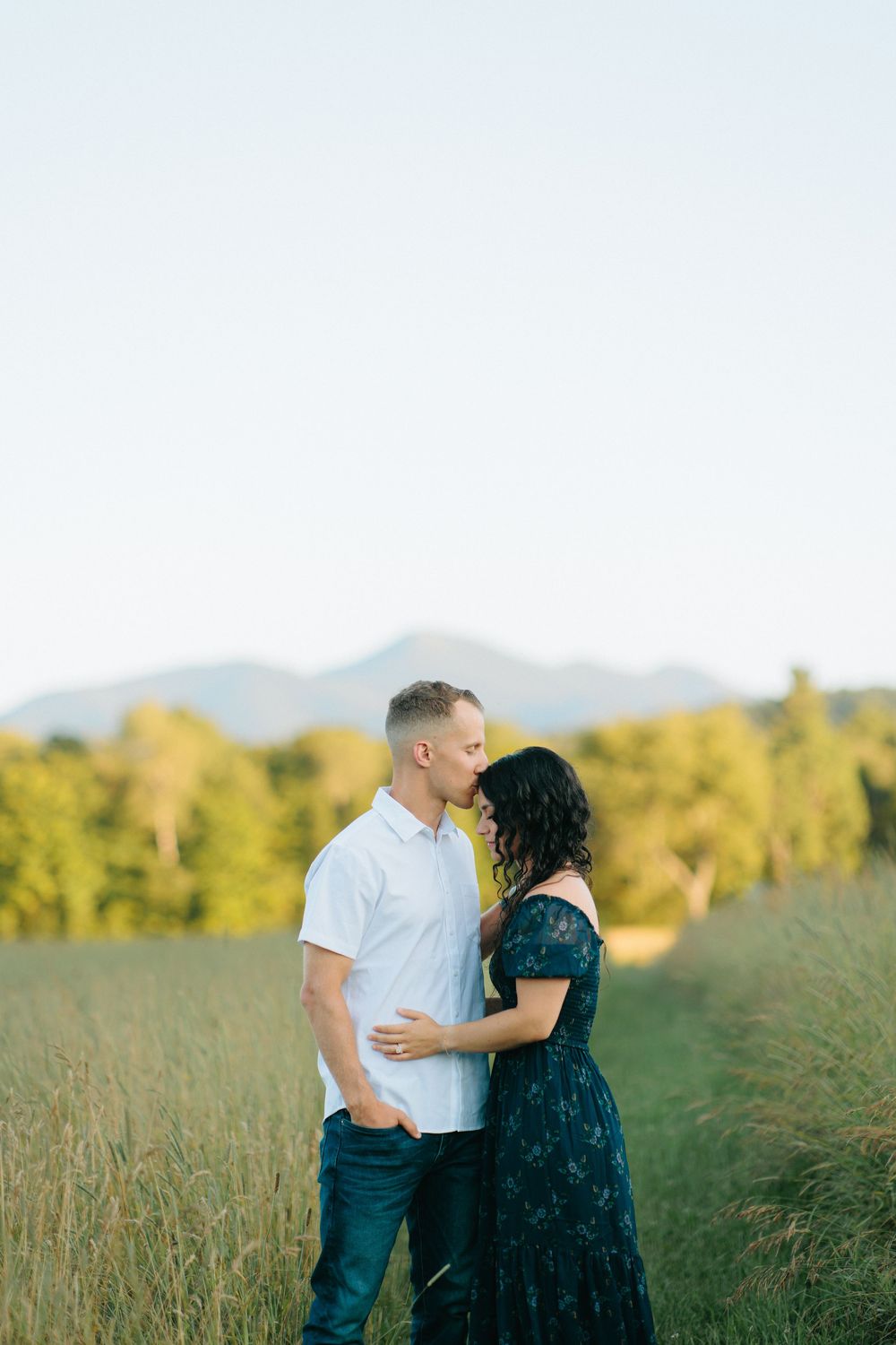 Romantic couple embraces in a scenic mountain meadow during golden hour.
