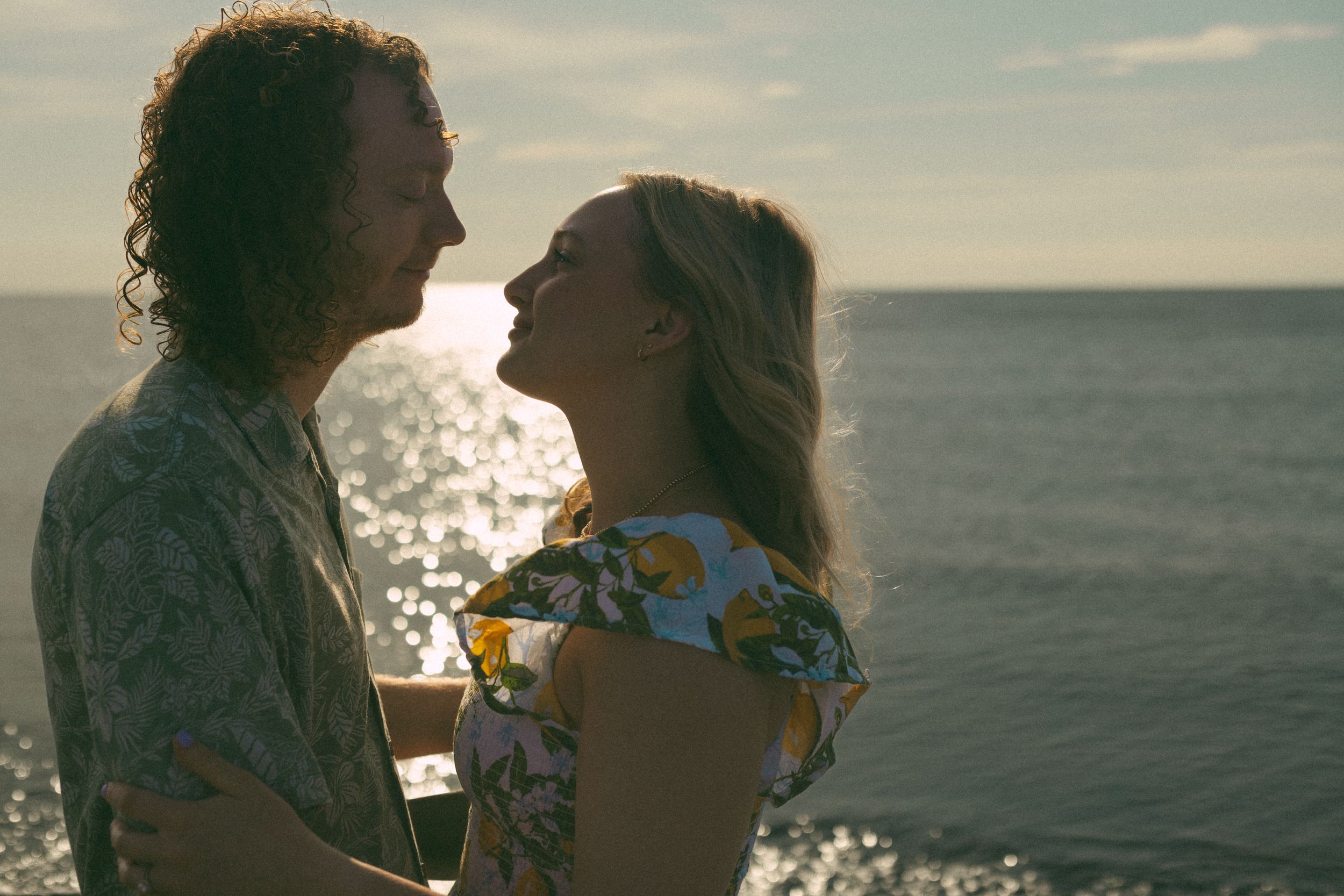 Romantic couple silhouetted against a sunlit ocean horizon during golden hour, sharing an intimate moment.