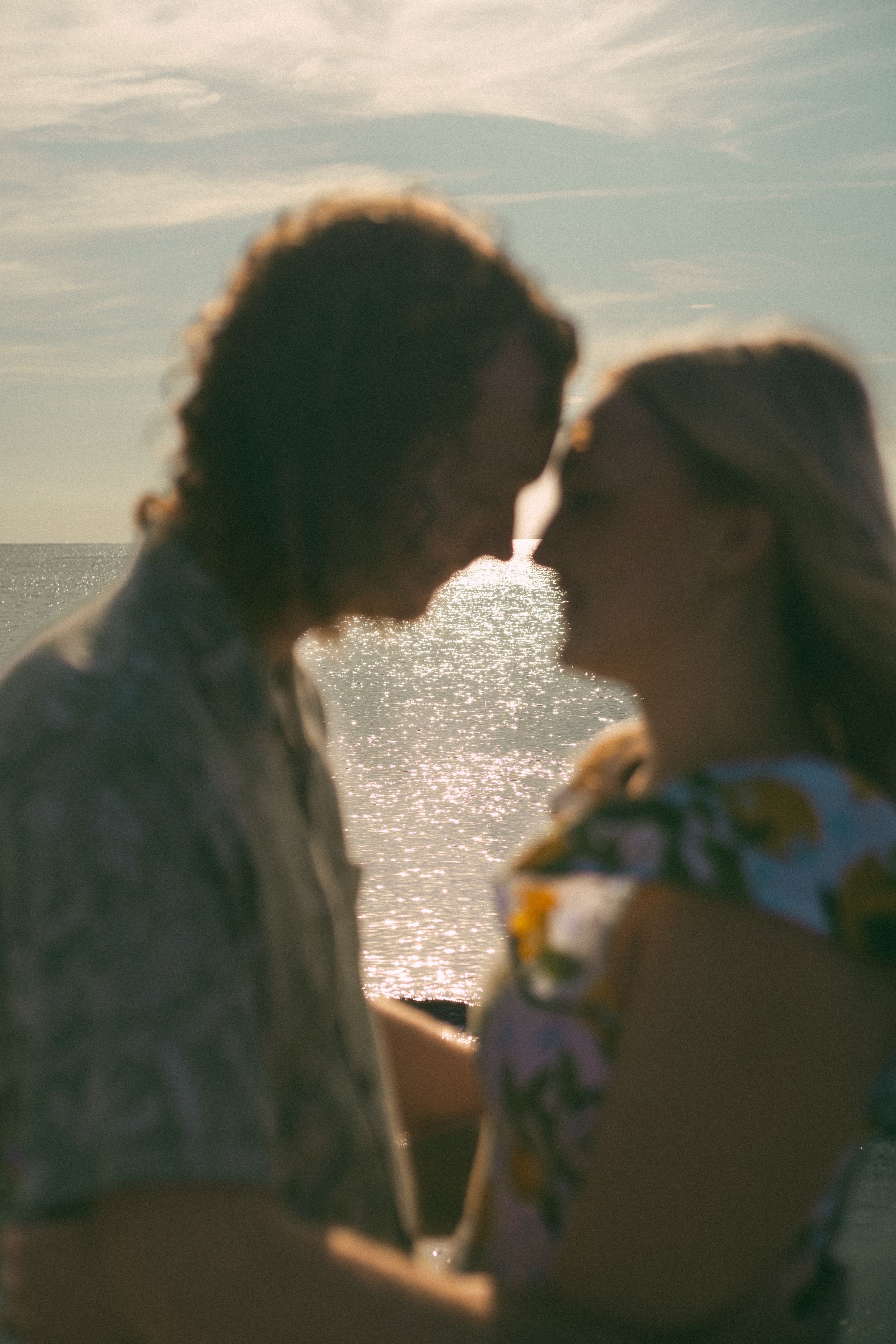 A backlit silhouette of a couple against sparkling ocean waters during a romantic sunset moment.