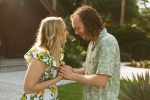 A couple wearing floral print outfits shares an intimate dance moment outdoors in a garden setting at sunset.
