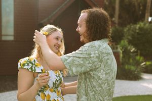 Two people share a joyful dance together outdoors in warm sunlight wearing vibrant yellow and sage green dresses.