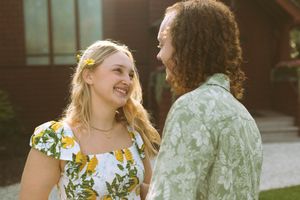 A couple in floral and sage green outfits stands together in warm evening sunlight during a wedding.
