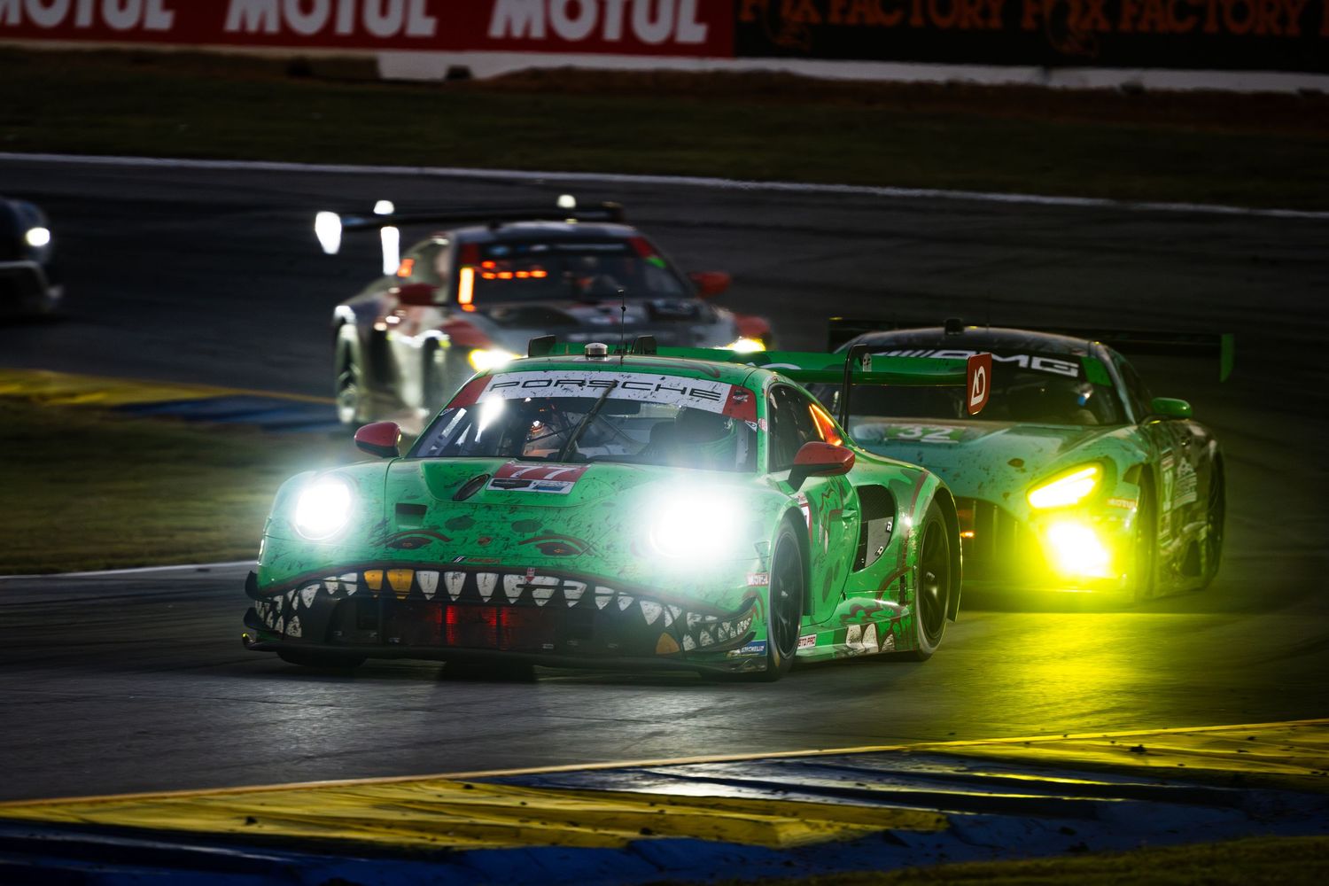 Race cars with bright headlights competing on a night track with Motul advertising visible.