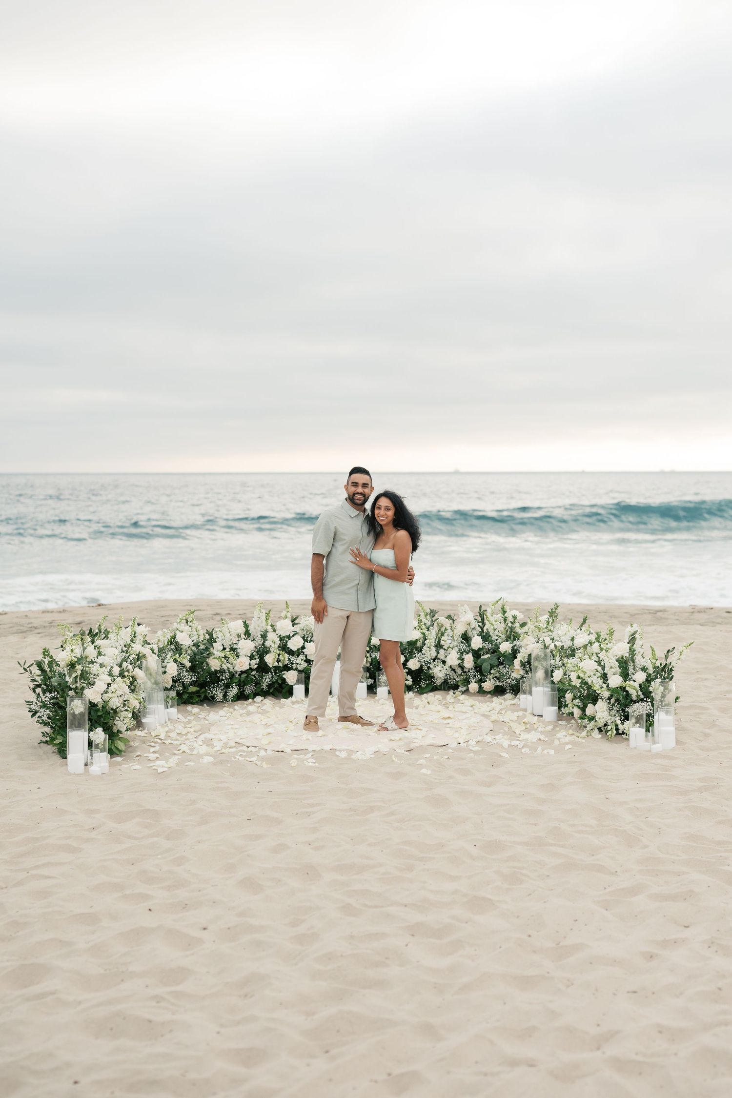 A romantic beach wedding proposal scene with floral decor and ocean waves in the background.