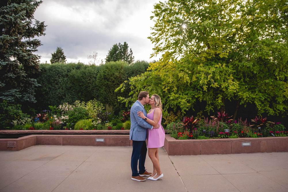 A couple shares a romantic moment against a backdrop of lush greenery in a beautiful garden setting.