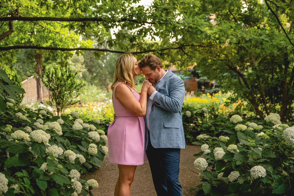 A romantic couple shares tender moments in a lush garden setting surrounded by flourishing hydrangea bushes and greenery.
