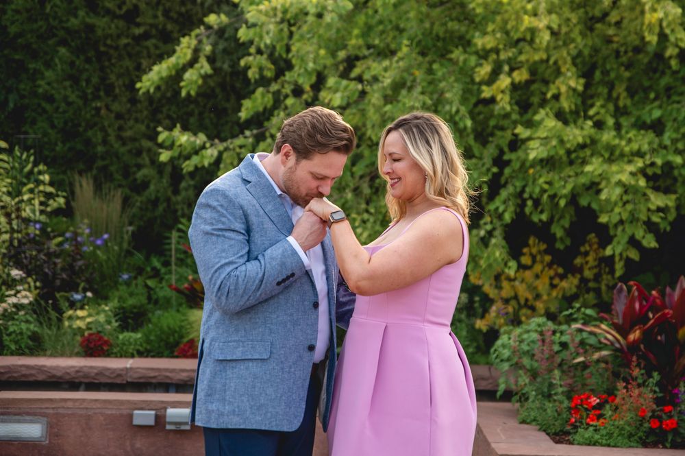 A couple shares tender moments in an outdoor garden setting wearing blue suit and pink dress.